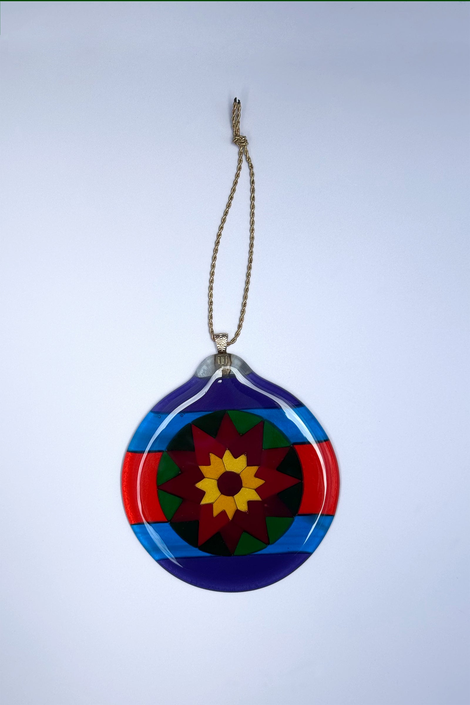 Fair Isle Poinsettia fused glass ornament on a white background, showing bold geometric design in purple, blue red green, orang and yellow art glass.
