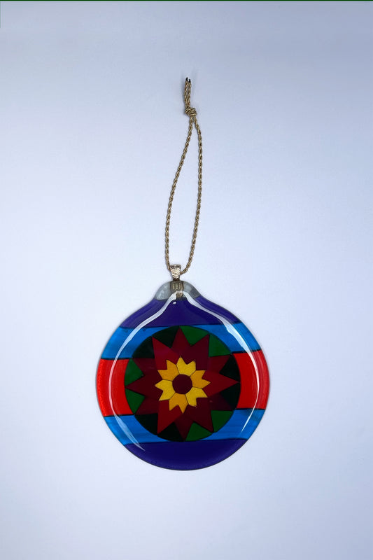 Fair Isle Poinsettia fused glass ornament on a white background, showing bold geometric design in purple, blue red green, orang and yellow art glass.