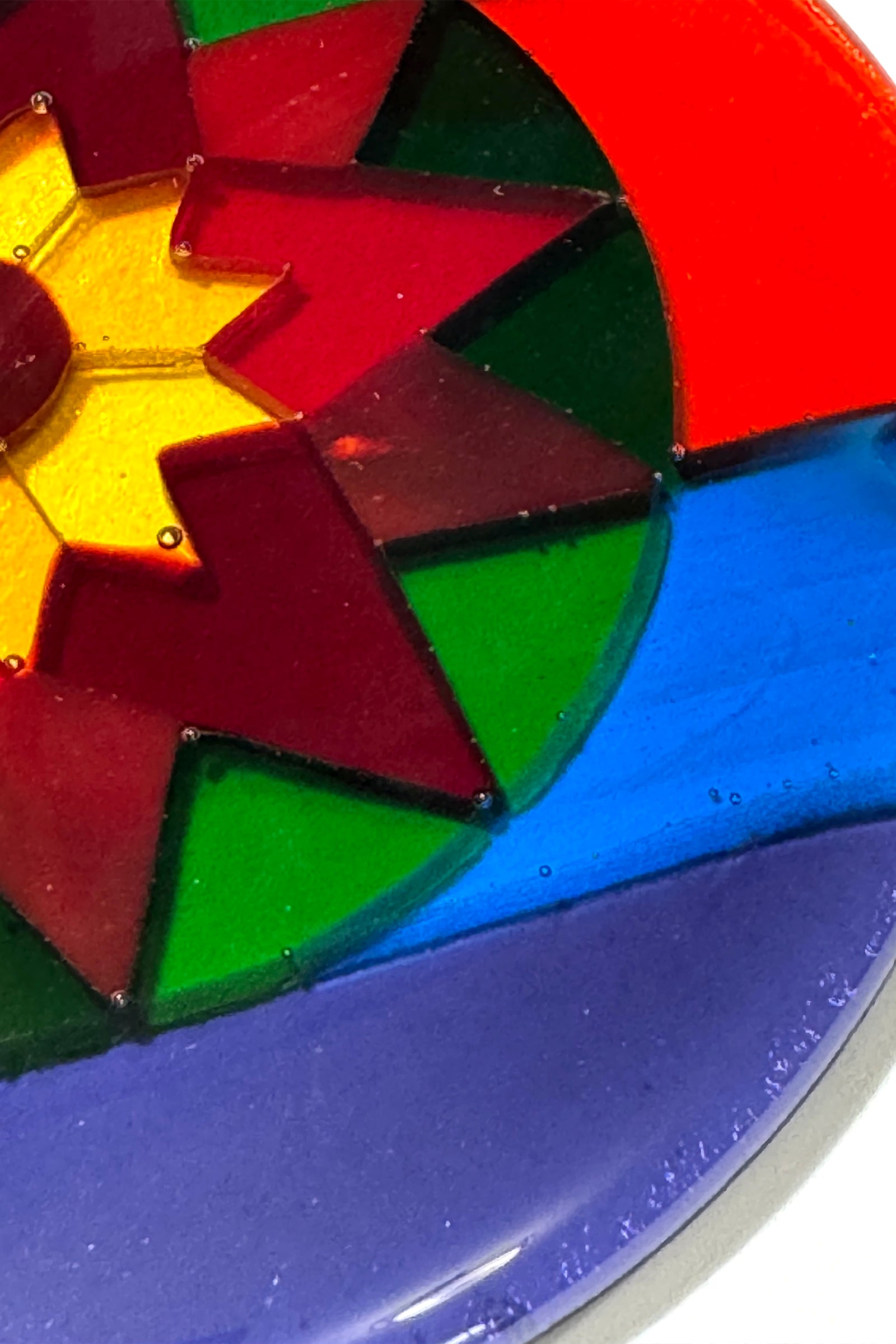 Close-up detail of hand-cut art glass pieces in the Fair Isle Poinsettia ornament, showing individual red, green, yellow, blue and purple glass segments fused together.