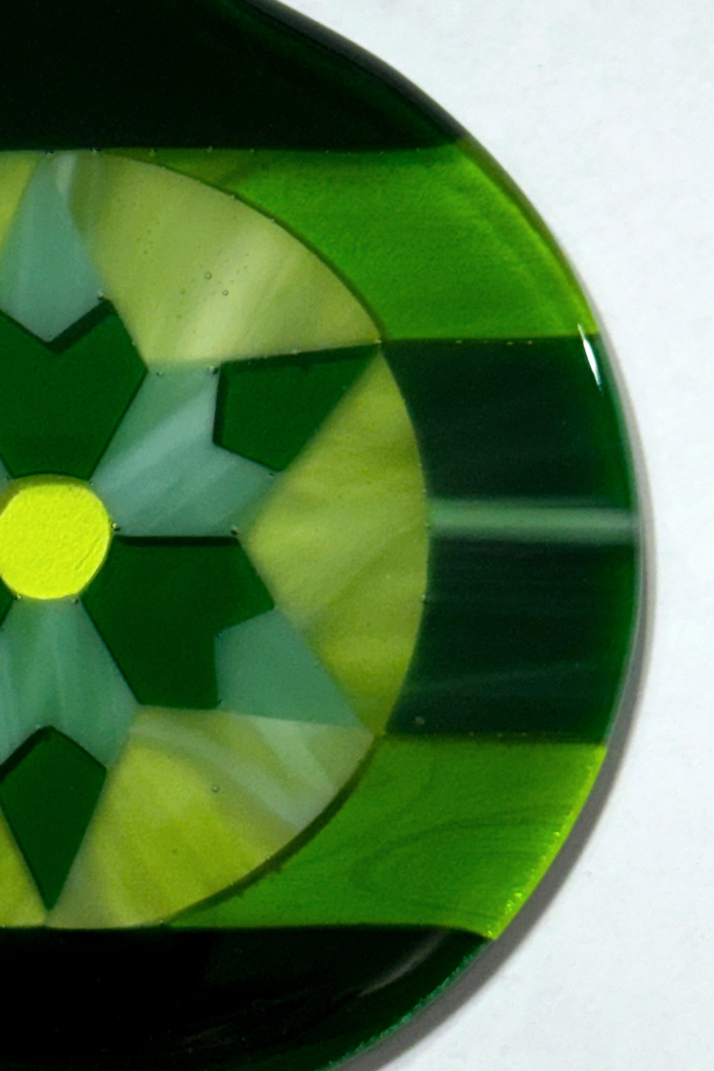 Close-up detail of hand-cut green art glass pieces and yellow center dot in a kiln-fired star ornament by AWinburnART.