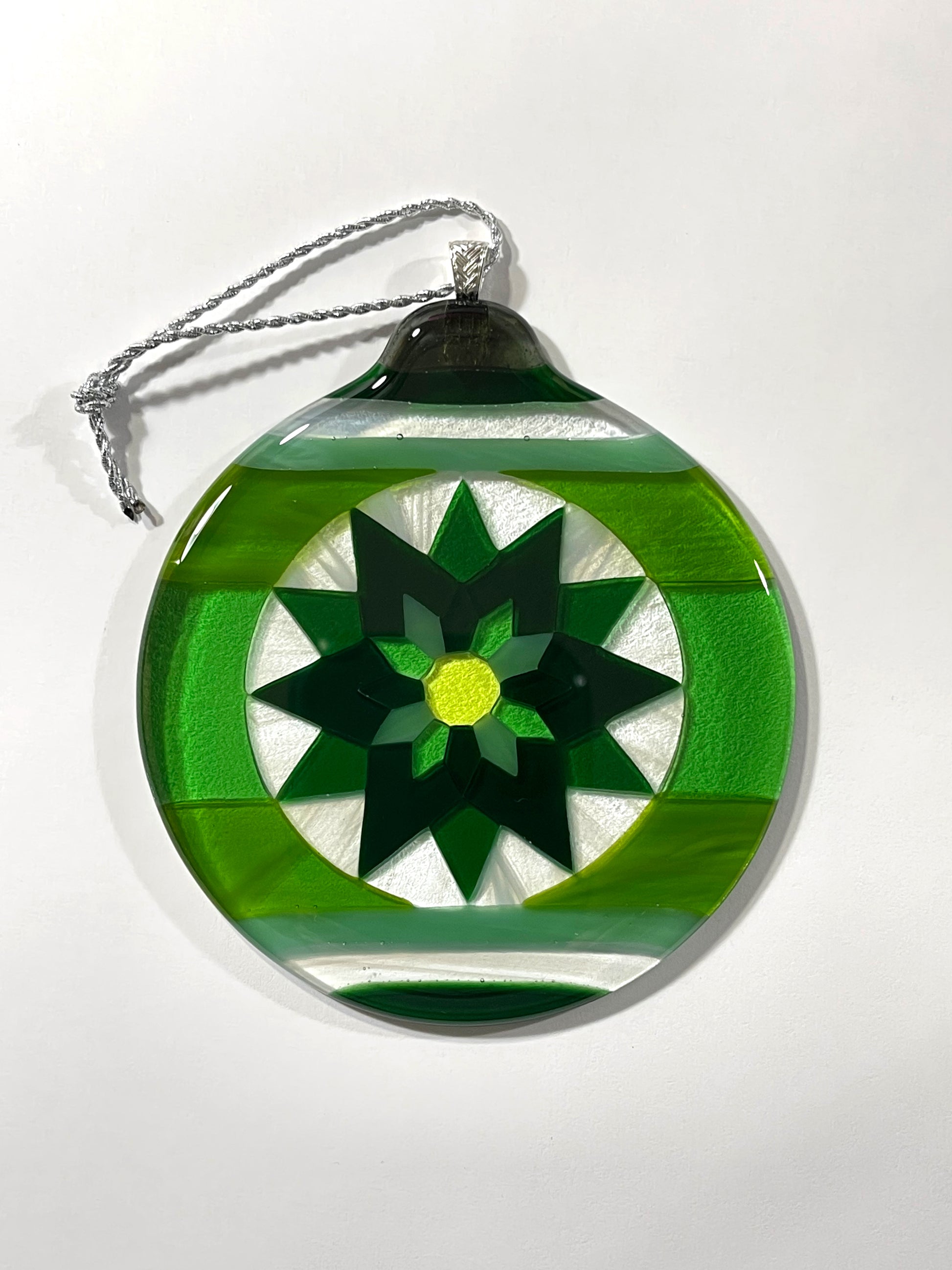 Green Fair Isle Poinsettia fused glass ornament in dark green, bright green, and white wispy with a yellow-green center on a white background.