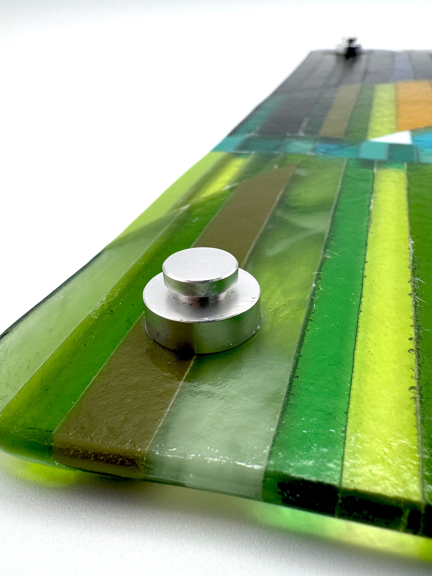 Close-up of Promise fused glass wall art by AWinburnART showing standoff mounting hardware on back and hand-cut glass edge detail 